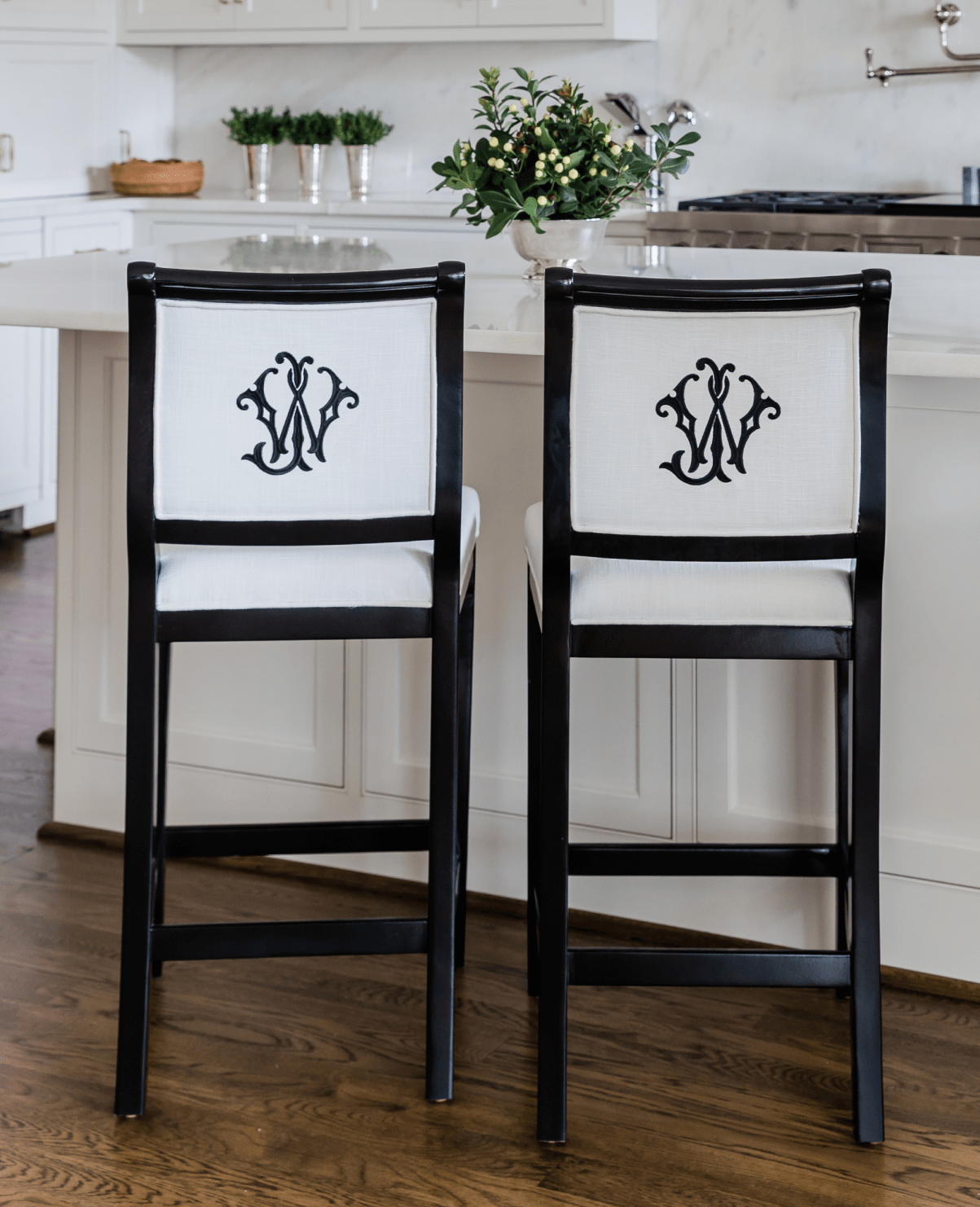 Two black and white counter height upholstered barstools at a kitchen island. Custom barstools are personalized on the back with a two-letter black embroidered monogram.