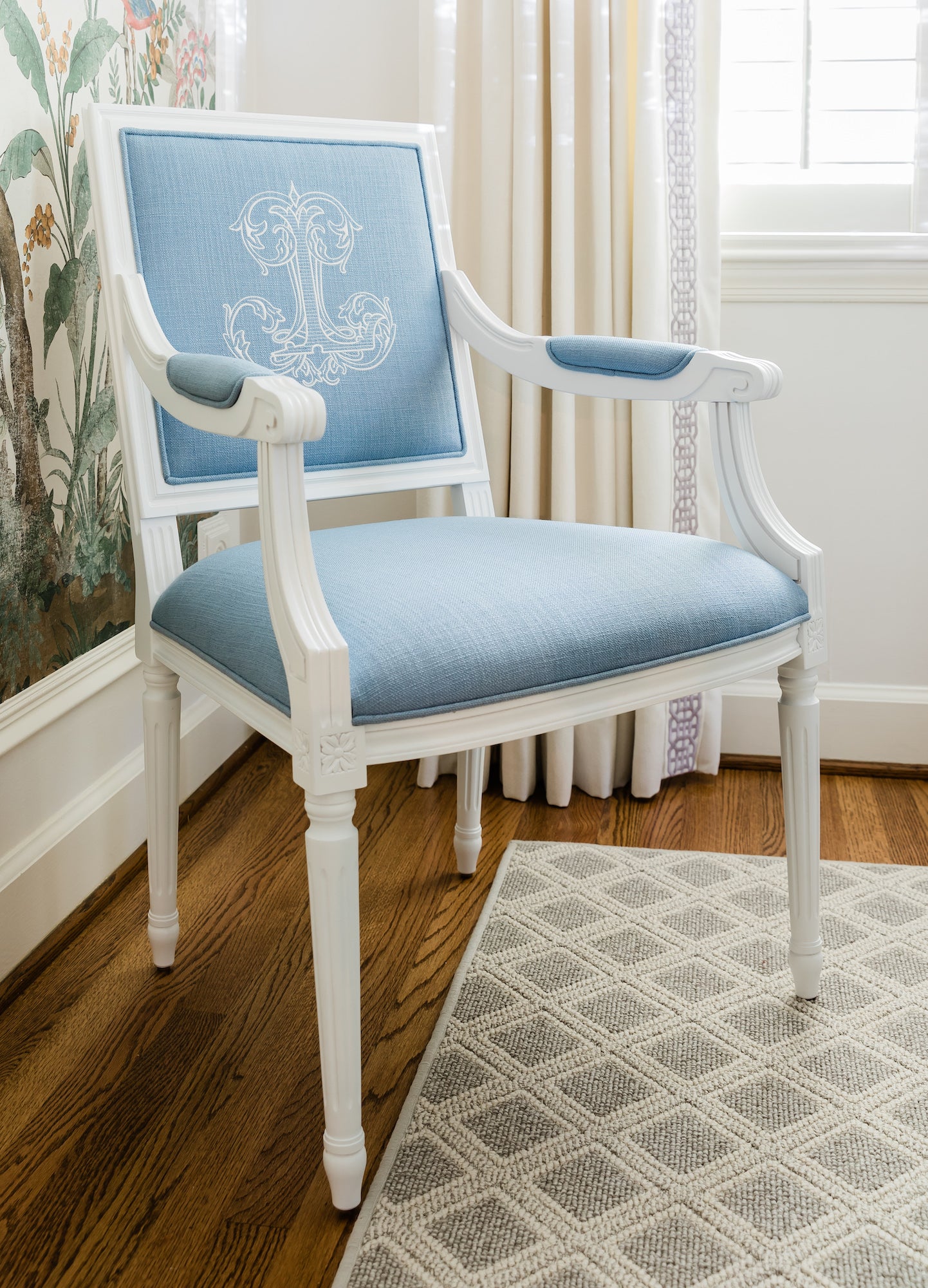 White, personalized King Louis XVI Square Back Arm Chair with chambray blue linen fabric and white embroidered monogram. Custom dining chair is in the corner of a Dining Room in front of a floral Gucci wallpaper panel.