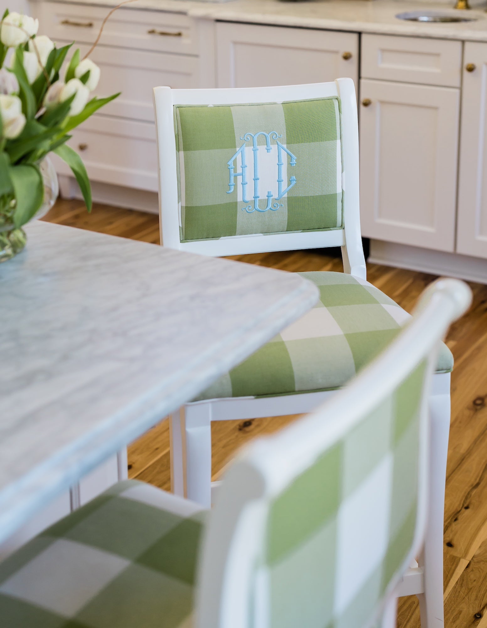 White, custom kitchen barstools with green and white buffalo check fabric. Personalized with a light blue chinoiserie style monogram on the inside back of the barstool.