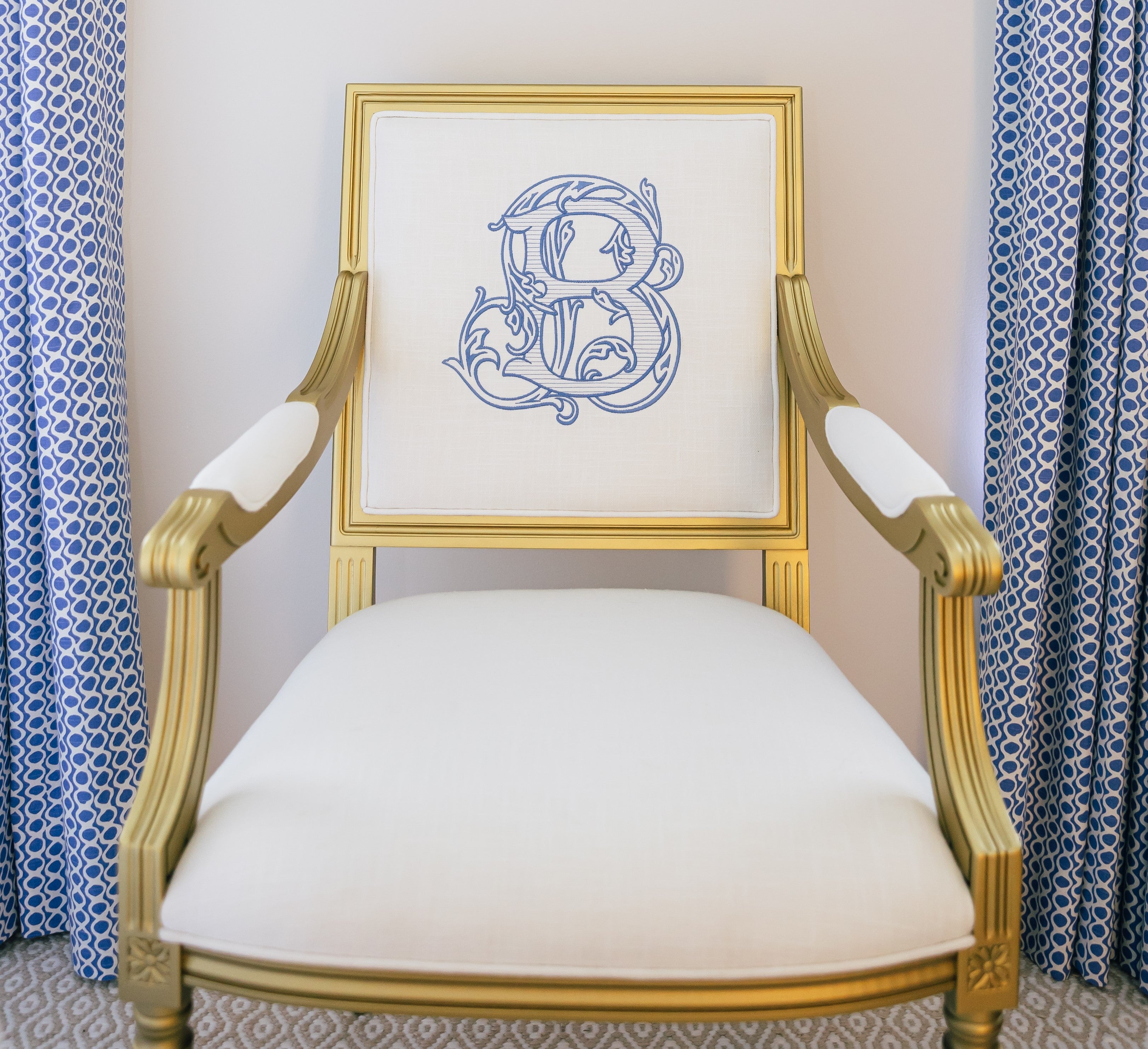 Gold Louis style custom arm chair. White linen fabric. Monogrammed chair back has a big royal blue scripty B.